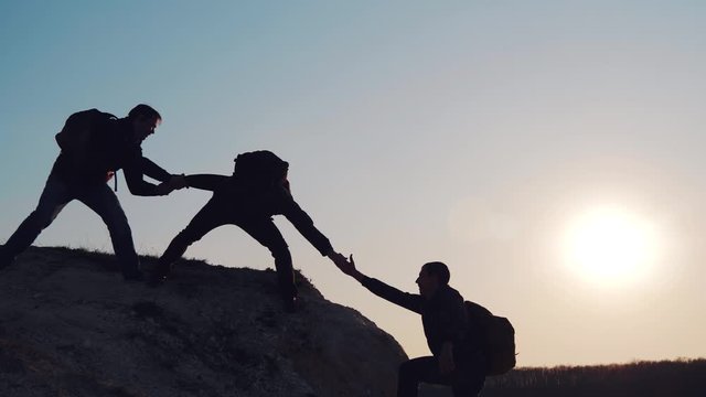At sunset, tourists climb the mountain, overcoming obstacles. Silhouettes of men helping each other in a difficult situation. A friend, a young man, gives a helping hand.