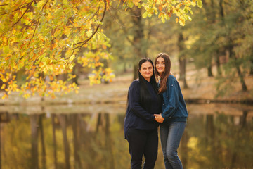 Fototapeta premium Mother with daughter stand in front of lake in the park. Yellow tree in autumn time