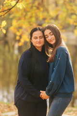 Mother with daughter stand in front of lake in the park. Yellow tree in autumn time