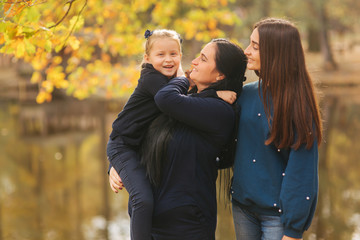 Mom with two daughter have fun in ther park. Youngest daughter collect leaves and smile. Happy family walking in the forest