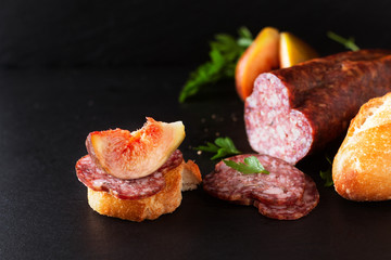 Food concept dried cured sausage on black slate board with copy space