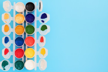 Multi-colored paint in cans on blue background. Palette of colors. Concept - creativity and school theme. Open jars of gouache paint, on a blue background.
