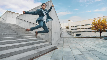 Cheerful and Happy Businessman in a Suit is Holding Coffee and Jumping While Walking Down the Stairs. Scene Shot in an Urban Concrete Park Next to Business Center. Sunny.