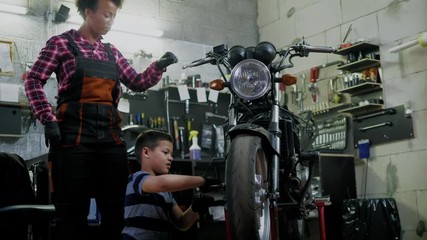 African american woman mechanic and boy helper repairing a motorcycle in a workshop