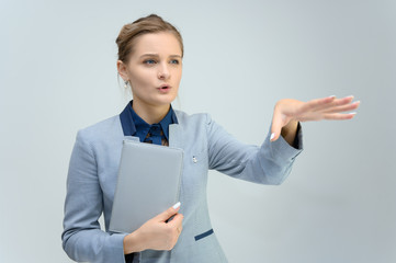 Studio photo a waist-high portrait of a cute young woman girl in a business suit on a white background with a folder in hands. He stands right in front of the camera, explains, with emotion.