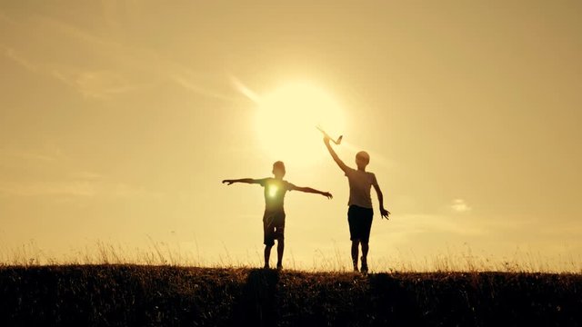 Two boys play with a wooden plane at sunset. Silhouette of children playing with an airplane. Dreams of flying. Children concept. Teamwork. Games and teamwork