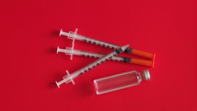 Insulin syringes and an ampoule of insulin hormone on a red background, close-up. Slow motion. Concept of immunization, insulin hormone, vaccination, cosmetic injection and health care.