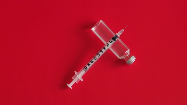 An insulin syringe with a needle and an ampoule of medicine or insulin on a red background, close-up. Slow motion. Type 1 diabetes.