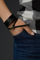 Cropped close-up shot of a female wrist with a multilayer bracelet made of long black leather strip...