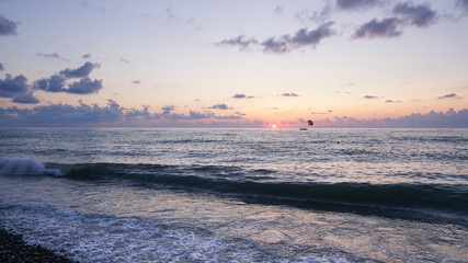 Parasailing in blue sea during orange evening sundown on horizon, beautiful scenery of tranquil seascape in summer evening twilights. Tourists on a parachute over the sea. Sunset paradise 