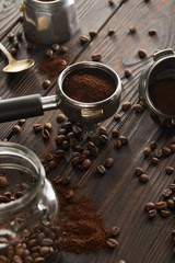 Portafilter near spoon, geyser coffee maker and glass jar with coffee beans on dark wooden surface