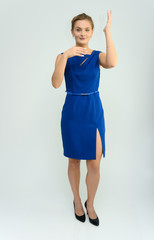 Full length studio portrait photo of a cute young woman girl in a beautiful blue dress on a white background. He stands right in front of the camera, explains with emotion.