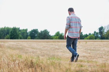 Naklejka na ściany i meble Depressed man walking alone across a field with his head held low