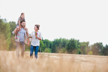 Young Caucasian family walking across field with young child on her fathers shoulders with the wife holding a bouquet of flowers