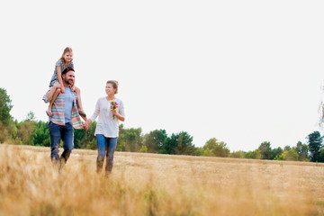 Young Caucasian family walking across field with young child on her fathers shoulders with the wife...