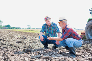 Mature farmer showing soil with senior farmer in field 