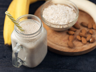Fresh banana smoothie on a wooden table in a jar . With oatmeal and almonds