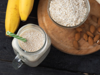 Fresh banana smoothie on a wooden table in a jar . With oatmeal and almonds