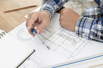 Architect working on a  blueprint. Casual man working on  blueprint and architecture model with pencil at office. 