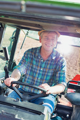 Smiling mature farmer driving harvest equipment in field