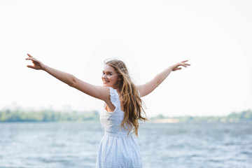 beautiful girl in white dress standing with hands in air and looking at camera