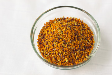 Bee pollen granules in a glass bowl on white background. Superfood. Copy space.