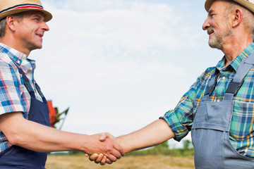Mature farmer hand shaking senior farmer in field