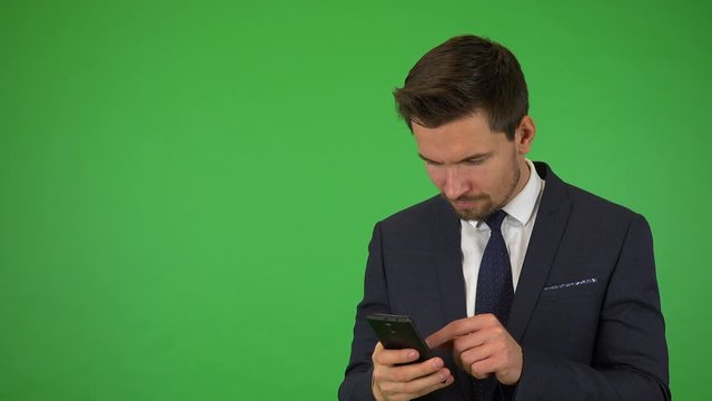 A young handsome businessman takes selfies with a smartphone - green screen studio