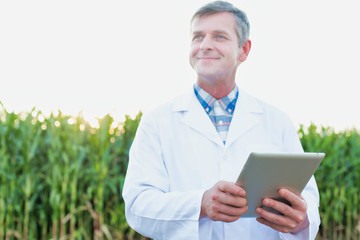 Smiling crop scientist using digital tablet while standing against corn field