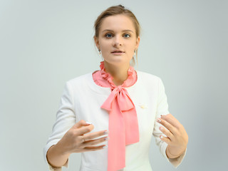 Photo studio portrait of a cute young woman girl in a beautiful suit of white-pink tender color on a white background. He stands right in front of the camera, explains with emotion.