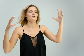 Fototapeta premium Photo studio portrait of a cute blonde young woman girl in a black blouse on a white background. He stands right in front of the camera, explains with emotion.