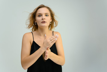 Photo studio portrait of a cute blonde young woman girl in a black blouse on a white background. He stands right in front of the camera, explains with emotion.