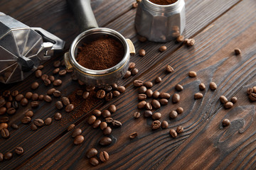 Geyser coffee maker near portafilter on dark brown wooden surface with coffee beans