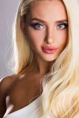 Naklejka premium Close-up portrait of sensuality young blonde girl with gray eyes, woman with stylish make up is looking flirty and smiling cute on gray wall background, beauty concept, free space