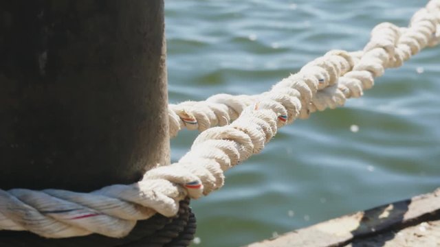 Close-up nautical knot rope tied around stake on boat or ship, boat mooring rope. Marine rope on the ship. The ship leaves the port.  Lighthouse. Mooring rope. Ship in the harbor.
