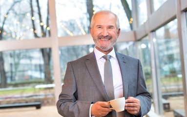 Confident businessman standing while drinking coffee in office