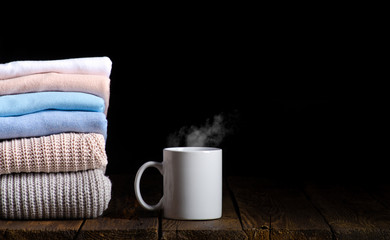 Fototapeta na wymiar stack of clothes from knitted knitwear with cup of tea, coffee on a wooden background, toned image