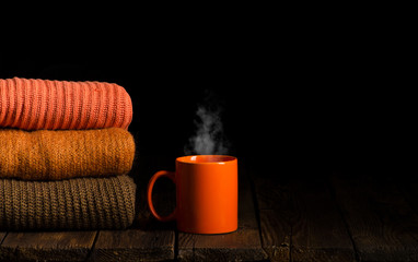 stack of clothes from knitted knitwear with cup of tea, coffee on a wooden background, toned image