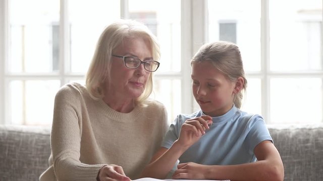 Elderly tutor or grandmother helps schoolchild or granddaughter with homework