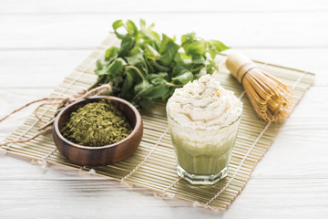 matcha green tea with whipped cream on bamboo mat with powder, mint and whisk