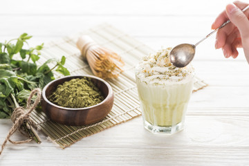cropped view of woman with matcha tea in glass with whipped cream