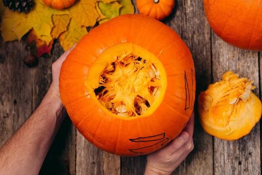 Hands opening Halloween pumpkin to clear it for carving to celebrate wooden table Trick or Treat horizontal