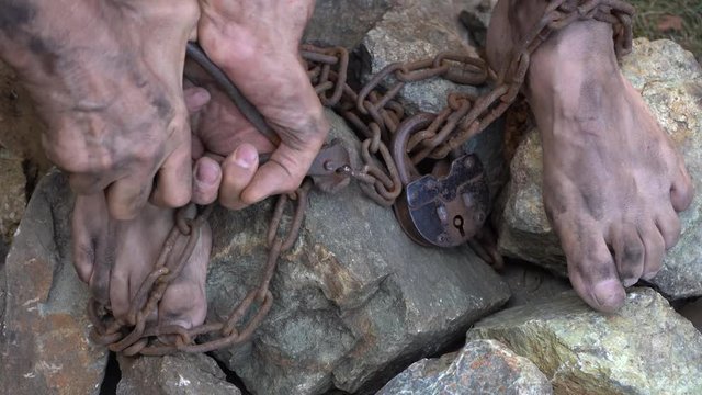 Hands and feet of a slave entangled in iron chains. An attempt to break free from slavery. The symbol of slave labor. Hands in chains