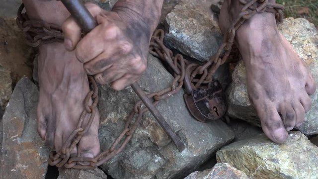 Hands and feet of a slave entangled in iron chains. An attempt to break free from slavery. The symbol of slave labor. Hands in chains.