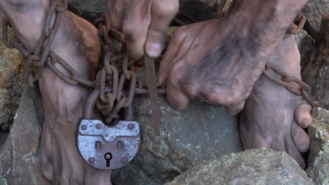 Hands and feet of a slave entangled in iron chains. An attempt to break free from slavery. The symbol of slave labor. Hands in chains.