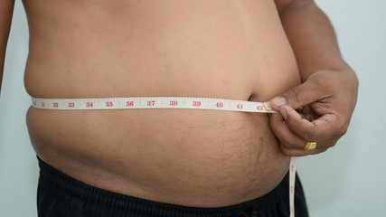 man measuring his fat belly with a measuring tape