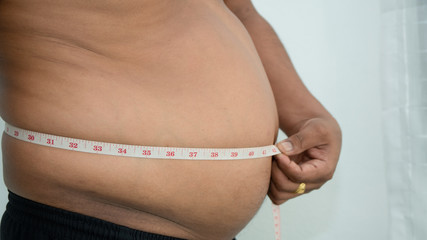 man measuring his fat belly with a measuring tape