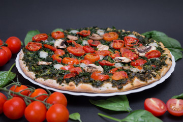 Pizza vegana con espinacas, tomates cherry y champiñones sobre fondo negro.