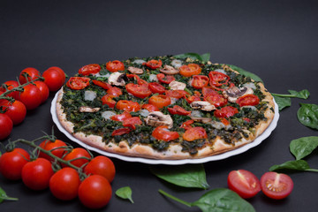 Pizza vegana con espinacas, tomates cherry y champiñones sobre fondo negro.
