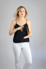 Fototapeta premium Full length studio portrait photo of a cute young blonde woman girl in a black blouse and white pants on a white background. He stands right in front of the camera, explains with emotion.